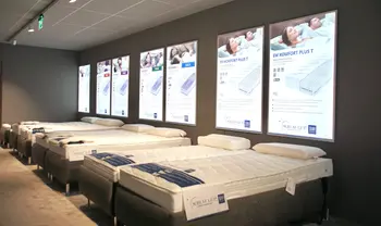 Matratzen-Ausstellung mit mehreren Betten und beleuchteten Informationsdisplays an der Wand, präsentiert in modernem Showroom mit gedämpfter Beleuchtung.